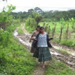 Young Mayan Q'eqchi' girls carrying sandals on muddy path